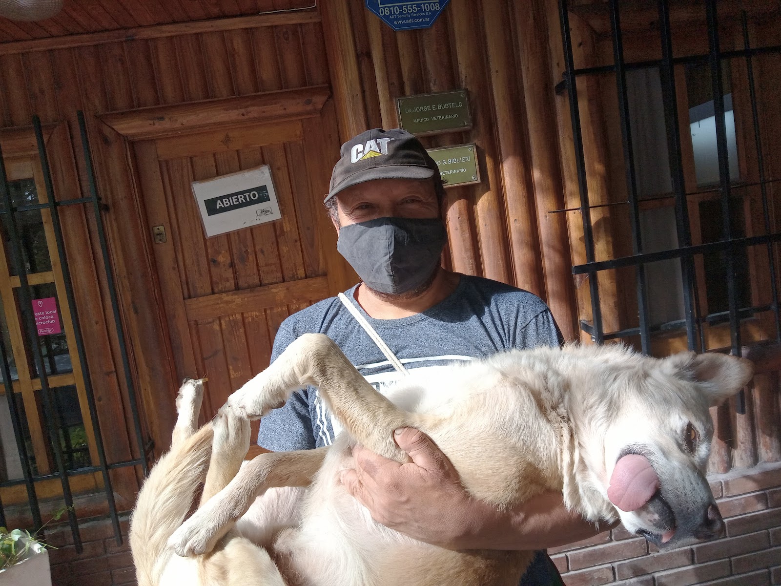 Dr. J. Jorge E. Bustelo en la entrada de la clínica con un perro grande, junto a las placas profesionales de Bustelo y Biglieri